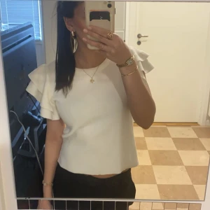 Vit topp med volangärmar - Säljer en stilren vit topp med volangdetaljer på ärmarna. Toppen har en normal passform och är perfekt för en chic look. Den är tillverkad i ett mjukt material som ger en bekväm känsla.