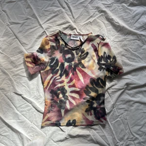 Färgglad blommig topp  - Säljer en färgglad topp från weekday med ett blommigt mönster i svart, rosa och gul. Toppen har korta ärmar och en tight passform