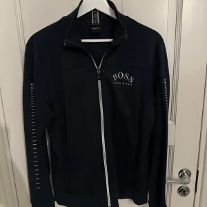 Mörkblå dress från Hugo Boss - Säljer en stilren mörkblå hoodie och mjukisbyxor från Hugo Boss. Perfekt för en avslappnad look. Kan säljas separat då kostar koftan 1000kr och byxorna 650kr Byxorna är i storlek M och koftan är i storlek S