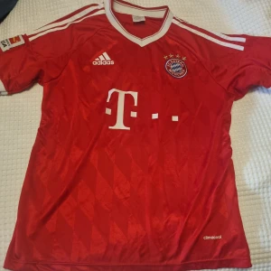 Röd fotbollströja från Adidas - Röd fotbollströja från Adidas med FC Bayern München-logga och vita detaljer.