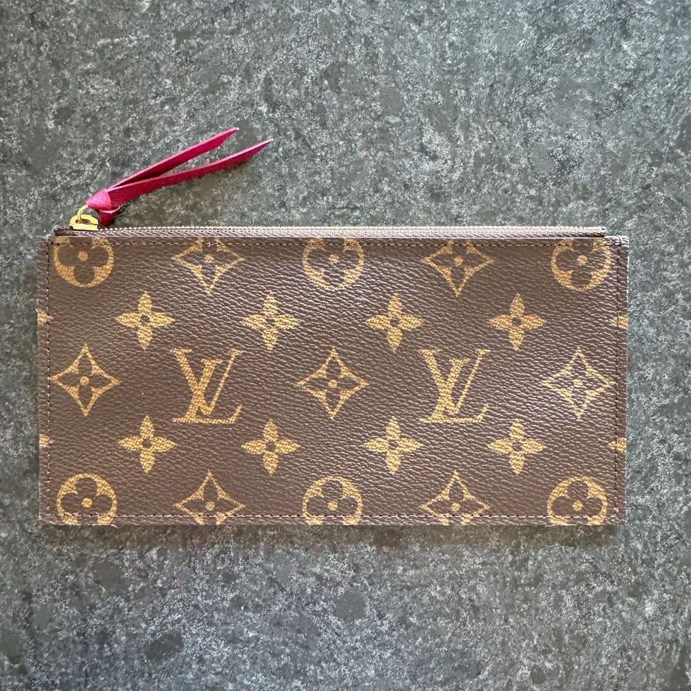 Säljer ett snyggt set bestående av plånbok och korthållare från Louis Vuitton. Plånboken har det klassiska monogrammönster med en rosa insida som matchar korthållaren med sin rosa färg. Plånboken har ett fack som stängs med en dragkedja. Korthållaren har 8 st kortfack och ett fack för exempelvis sedlar eller kvitton. Perfekt för att hålla ordning på dina kort och kontanter. Original dustbag medföljer i priset. Mått: 10x19 cm. . Laukut & Käsilaukut.