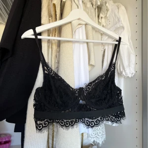 Svart spets bralette - Säljer en elegant svart spets bralette med justerbara axelband. Den har vackra spetsdetaljer och en bred kant nedtill för extra komfort. Perfekt för att lägga till en touch av lyx till din garderob.