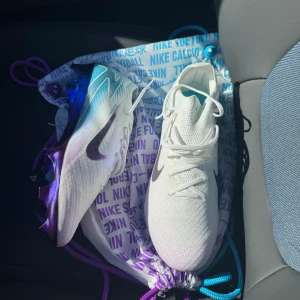 Nike fotbollsskor med lila detaljer - Säljer ett par oanvända Nike fotbollsskor Skorna har en modern design med snörning och en iögonfallande sula i lila och blått. Perfekta för fotbollsplanen!