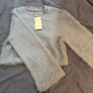 Grå fluffig tröja från Zara - Säljer en supermjuk och fluffig grå tröja från Zara. Den har en croppad passform och långa ärmar, perfekt för kyliga dagar. Tröjan är både stilren och bekväm, ett måste i garderoben! 🩶