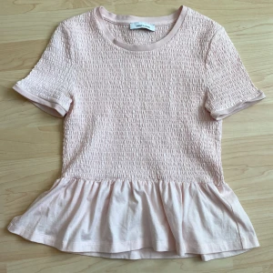 Ljusrosa smockad topp från Samsøe Samsøe - Söt ljusrosa topp från Samsøe Samsøe med smockdetaljer och volang nedtill. Storlek står inte på toppen men jag skulle anta att det är en  XS. 