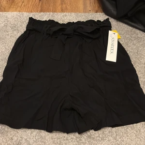 Svarta shorts - Snygga svarta shorts i storlek S. De har en högmidjad design med knytband i midjan för en justerbar passform. Köpte på Ullared men aldrig använt. 
