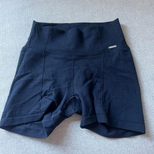 Marinblå  träningsshorts - Säljer ett par svarta träningsshorts med rätt så låg midja. De är tillverkade i ett syntetmaterial med en texturerad yta. Perfekta för gymmet eller löprundan! Villig till att sänka priset!