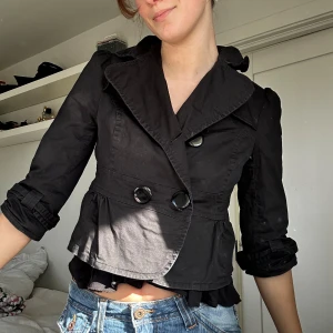 Trekvartsärmad kappa - Snygg svart kavaj från Orsay med stora knappar och trekvartsärmar. Den har en figursydd passform och en elegant krage. Perfekt för att ge en stilren look till din outfit.