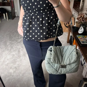 Quiltad axelväska i jeans - Snygg quiltad axelväska i ljusblått jeansmaterial med kedjerem. Väskan har ett stilrent spänne framtill och ett mjukt, vadderat utseende. Perfekt för att ge din outfit en cool touch.