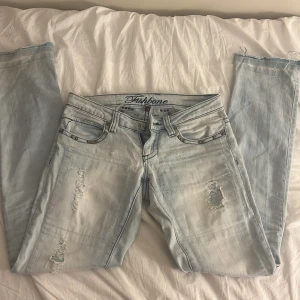 Ljusblå jeans med nitar från Fishbone - Snygga ljusblå jeans från Fishbone med slitna detaljer och coola nitar på bakfickorna. De har en klassisk femficksdesign och dragkedja. Perfekta för en trendig look! Midjemått: 38 cm innerbenslängd: 72 cm Skulle gå att sänka pris