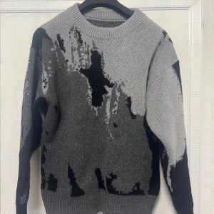 Grå och svart mönstrad tröja - Säljer en cool grå tröja med abstrakt svart mönster. Tröjan har en rund hals och långa ärmar, perfekt för en stilren look. Den är tillverkad i ett mjukt material som känns skönt mot huden.