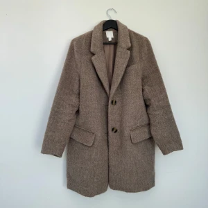 Beige kappa från H&M - Säljer en stilren beige lite baggy kappa från H&M. Den har en klassisk design med två knappar framtill och fickor på sidorna ❤️‍🔥