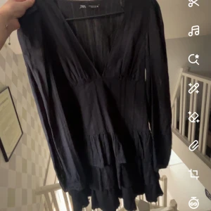 Svart klänning från Zara - Snygg svart klänning från Zara med v-ringning och långa ärmar. Perfekt för en stilren look. Klänningen har en lätt volangdetalj som ger en fin touch. Tror inte den går att köpa längre 
