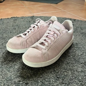 Rosa sneakers från Adidas - Snygga rosa sneakers i mocka från Adidas med klassisk design och vit sula. Perfekta för en avslappnad stil med snörning framtill.