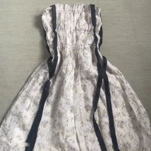 Blommig klänning från Brock Collection x H&M - Charmig blommig klänning från Brock Collection x H&M med smockdetaljer och svarta band. Perfekt för en romantisk look med sin ljusa färg och subtila blommönster.