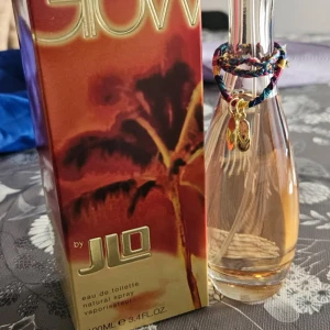 Glow by JLO Eau de Toilette - Säljer en flaska Glow by JLO Eau de Toilette. Flaskan har en elegant, kurvig design med ett färgglatt armband och en liten charm. Doften är fräsch och feminin, perfekt för dagligt bruk. Förpackningen har en tropisk design med palmer.