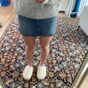 Blå jeanskjol - Säljer en snygg blå jeanskjol med klassisk design. Kjolen har en kort längd och en normal passform, perfekt för en avslappnad stil. Den har fickor fram och bak samt en dragkedja och knapp framtill.