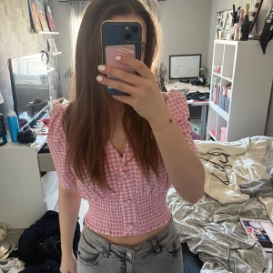 Rutig rosa blus med puffärmar - Säljer en söt rosa och vit rutig blus med puffärmar och v-ringning från Gina. Blusen har knappar framtill och en smockdetalj i midjan som ger en fin passform. Perfekt för vår och sommar! Den är storlek M men skulle mer säga att den känns som en S 😇. Använd enstaka gång 