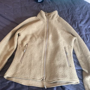 Grön ( den ser beige ut på bilden) fleecejacka från 157 - Säljer en mysig grön fleecejacka från 157. Jackan har en dragkedja framtill och två praktiska fickor med dragkedjor. Perfekt för kyliga dagar och ger en skön och varm känsla. Passar bra för både vardag och utomhusaktiviteter.
