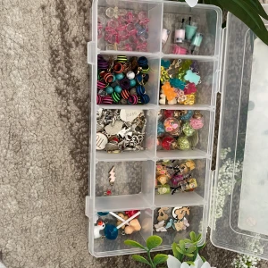 Samling av färgglada berlocker och pärlor - En samling av olika berlocker och pärlor i en praktisk förvaringslåda. Innehåller hjärtformade rosa pärlor, randiga kulor i olika färger, små flaskor med färg, och olika metallberlocker. Perfekt för smyckestillverkning eller pyssel. Säljer för 100kr då detta sammanlagt kostade mig ca 550kr, priset går absolut att diskutera så tveka inte att skriva till mig!❤️(allt i boxen ingår) man kan även få med annat till small business om man vill, då jag har slutat sälja smycken❤️