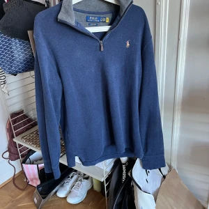 Blå tröja med dragkedja från Ralph Lauren - Säljer en stilren blå tröja från Ralph Lauren med dragkedja och broderad logga på bröstet. Perfekt för en avslappnad men snygg look. Tröjan har långa ärmar och en bekväm passform.