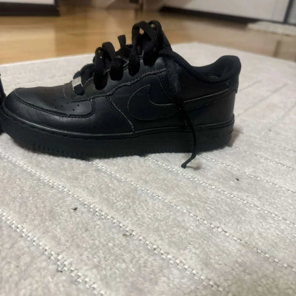 Säljer ett par klassiska svarta Nike Air Force sneakers. Skorna har en stilren design med snörning och den ikoniska Nike-loggan på sidan. Perfekta för en casual look.. Kengät.