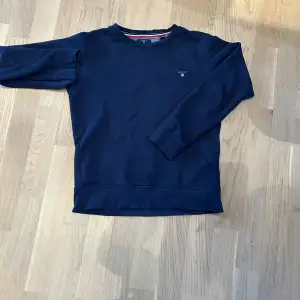 Säljer en stilren mörkblå tröja från GANT. Tröjan har en rund halsringning och ett diskret GANT-logotyp på bröstet. Perfekt för en avslappnad och snygg look.