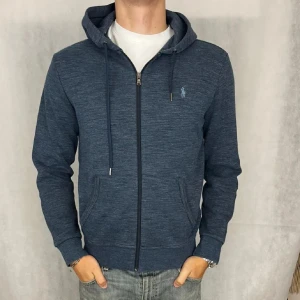 Blå hoodie från Polo Ralph Lauren - Säljer en snygg blå hoodie från Polo Ralph Lauren med dragkedja. Tröjan är långa ärmad. Perfekt för en avslappnad stil.