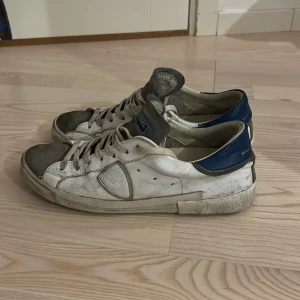 Vita sneakers från Philippe Model - Snygga vita sneakers från Philippe Model med grå detaljer och blå häl. Skorna har snörning och en rund tå, vilket ger en klassisk look. Perfekta för en avslappnad stil. Skorna kommer direkt från skomakaren och är helt nyrenoverade!