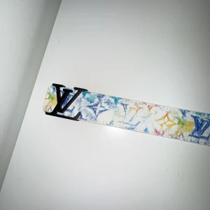 Färgglatt bälte från  - Säljer ett stilrent bälte från pänne. Bältet har en vit bas med inslag av blått, gult och orange. Perfekt för att ge en färgklick till din outfit.