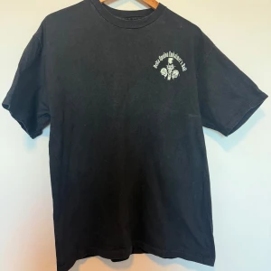 Svart t-shirt från Hanes - Säljer en svart t-shirt från Hanes med tryck på både fram- och baksidan. Framsidan har en liten vit text och grafik, medan baksidan har ett större tryck med text och en illustration. Perfekt för dig som gillar unika tryck!