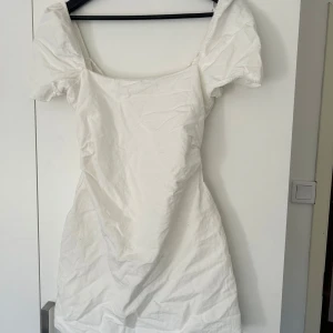 Vit klänning från Zara - Säljer en stilren vit klänning från Zara med korta puffärmar och en öppen rygg med snörningsdetalj. Perfekt som studentklänning