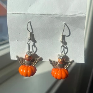 Örhängen med pumpa och änglavingar - Unika örhängen med orange pumpa och silverfärgade änglavingar. Perfekta för höst och Halloween. Knappt använda. 