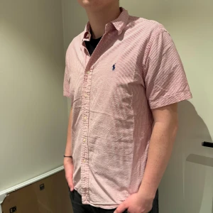Ralph Lauren T-Shirt Skjorta - Superfin T-Shirt skjorta från Ralph Lauren! Skjortan är i nyskick och har ett unikt utseende, med korta ärmar och vit rosa ränder! Storlek L! Priset är inte hugget i sten! har ni några fler frågor är det bara att skicka ett PM! Mvh