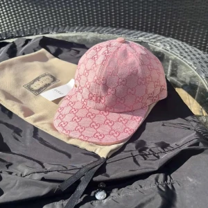 Rosa keps från Gucci - Snygg rosa keps från Gucci med det ikoniska GG-mönstret. Kepsen har en justerbar rem baktill för perfekt passform. Perfekt för att ge din outfit en lyxig touch.