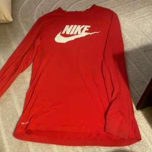 Röd långärmad tröja från Nike - Säljer en röd långärmad tröja från Nike med vit logga på bröstet. Perfekt för en sportig look eller avslappnade dagar. Tröjan är tillverkad i ett mjukt och bekvämt material.