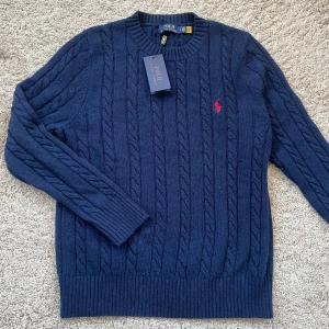 Mörkblå stickad tröja från Polo Ralph Lauren - Snygg Polo Ralph Lauren kabel stickad tröja i mörkblå färg. Helt ny, aldrig använd och i perfekt skick! Storlek L men passar även M. Tveka inte att höra av er om ni har några frågor!