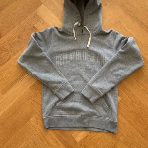 Grå hoodie från Replay - Säljer en snygg grå hoodie från Replay med tryck på framsidan. Den har en klassisk känguruficka och justerbar huva med snören. Perfekt för en avslappnad stil.