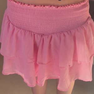 Rosa volangkjol - Söt rosa kortkjol med volanger och elastisk midja. Perfekt för en somrig look. Kjolen har en luftig design som ger en lekfull känsla.