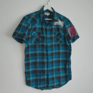 Rutig kortärmad skjorta från Diesel - Snygg rutig skjorta från Diesel i blått och svart med korta ärmar. Skjortan har knappar framtill och två bröstfickor med lock. Perfekt för en avslappnad stil.