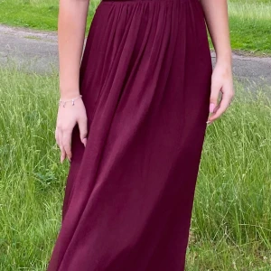 Vinröd långklänning från NLY Eve - Supersnygg vinröd långklänning från NLY Eve med öppen rygg och knyt i midjan. Klänningen har smala axelband som korsas i ryggen och ett flowy fall. Tillverkad i 100% polyester, perfekt för sommarkvällar eller bal.