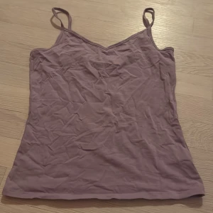 Lila linnetopp med smala axelband - En enkel och stilren lila linnetopp med smala axelband och v-ringad hals. Perfekt att matcha med jeans eller kjol för en avslappnad look. 