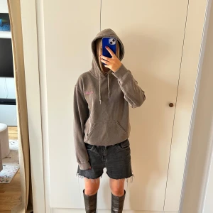 ljusbrun hoodie från Urban Outfitters - Ljusbrun tvättad hoodie från Urban Outfitters med en liten rosa broderad text på bröstet. Tröjan har huva med snörning, känguruficka och lång ärm. Perfekt för chill dagar och enkel att matcha med jeans eller shorts. Jag är 158cm för referens.
