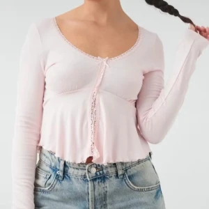 Ljusrosa blus med spets från Gina Tricot - Supersöt ljusrosa blus från Gina Tricot med lång ärm, v-ringning och spetsdetaljer längs kanterna. Blusen har en liten rosett framtill och volangig nederkant. Säljer pga kommer inte till användning, använd en-två gånger. Nypris: 260kr