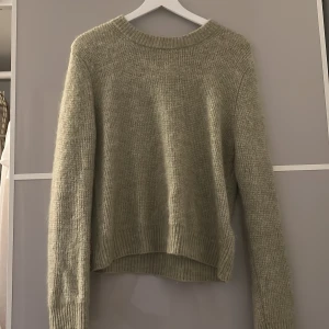 Beige stickad tröja med rund hals - Mysig stickad tröja i grön med rund halsringning och långa ärmar. Tröjan har ribbade muddar vid ärmslut och nederkant, perfekt för lager på lager under kyliga dagar. Enkel och stilren design som passar till det mesta.