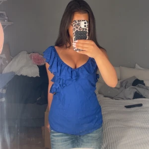 Blå volangblus från Yessica - Supersöt blå blus från Yessica med djup v-ringning och volangdetaljer. Funkar perfekt till jeans eller kjol. Toppens material känns lätt och flowy, vilket gör den extra bekväm. Bara att dm:a vid frågor eller funderingar!💕