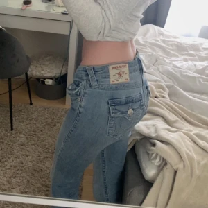 True Religion ljusblå bootcut jeans - Säljer ett par ljusblå jeans från True Religion med snygga detaljer på bakfickorna. Modellen har bootcut och låg midja, modell joey, storlek 25/32