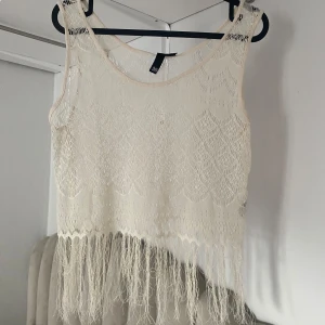 Vit beach cover up med fransar - Superfin cover up från H&M Divided med spetsmönster och långa fransar nertill. Toppen är ärmlös och har en luftig, bohemisk vibe som passar perfekt till sommaren. Snygg att styla med jeansshorts eller kjol för en chill look. Aldrig and vänd! Det är bara fråga om fler bilder eller mått💗💗
