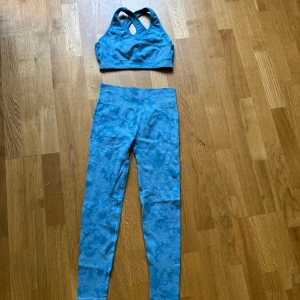 Blå camo träningstopp med korsrygg & matchade tights  - Säljer en blå träningstopp med camouflagemönster och snygga korsade axelband i ryggen med matchande tights. Toppen är ärmlös och har en sportig, tight passform som sitter på plats under träningen. Perfekt för gymmet eller löprundan!