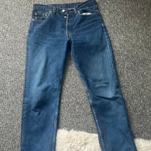 Levi's 501 blå jeans 32/32 - Klassiska Levi's 501 jeans i blå denim med raka ben och normal passform. Byxorna har fem fickor, knappgylf och den ikoniska röda Levi's-taggen på bakfickan. Tillverkade i bomull och perfekta för en avslappnad stil. Köpta second hand därav de billiga priset. Säljer då de var för små. W:32 L:32
